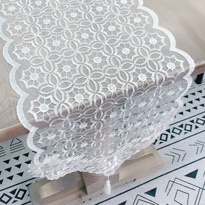 White lace table runner with scalloped edges and tassels on a light wood dining table