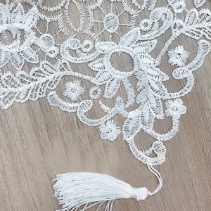 White lace table runner with clover floral embroidery and silk tassels on wood surface