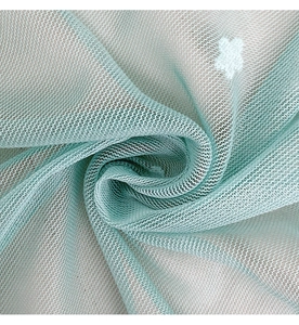 Vista macro di una tenda in tulle verde chiaro con motivi di fiori e stelle bianchi