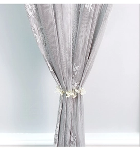 Dettaglio di un elegante fermatenda con perle bianche su una tenda in pizzo grigio