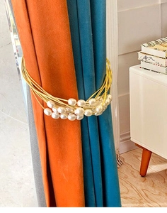 Detail of gold multilayer wire curtain tieback with white pearls on velvet drapes