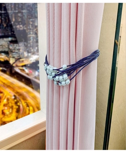 Detail of blue braided curtain tieback with white pearls on soft pink fabric