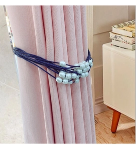 Detail of blue woven curtain tieback with faux pearls on pink fabric background