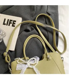 Détail du cabas vert avocat en cuir texturé avec un pendentif nœud en dentelle perlé