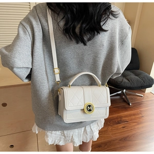 Detail of white quilted crossbody bag with golden M metal buckle on a shoulder strap