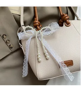 Détail du sac beige avec poignée en corde marron, nœud en dentelle et perles