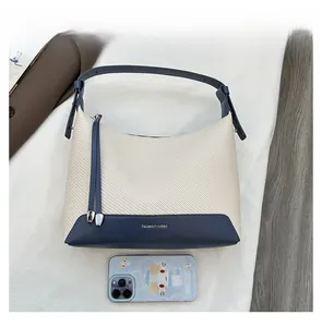 Detail view of woven underarm bag with blue leather trim beside a smartphone for scale