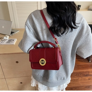 Macro shot of luxury burgundy quilted handbag featuring a gold M letter logo twist lock