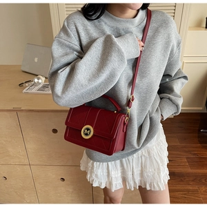 Detail of deep red quilted crossbody bag with golden M buckle on home background