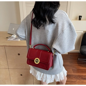 Detail of red quilted leather handbag with gold M-logo buckle shown on a shoulder