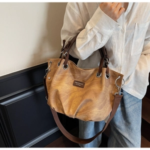 Detail view of a vintage caramel tote bag featuring textured leather and a logo leather patch