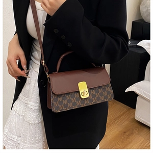Detail of a brown shoulder bag with letter M monogram print and golden metal clasp lock