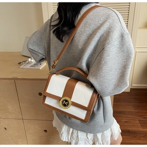 Detail of a quilted color-block handbag with a gold M-buckle and adjustable strap