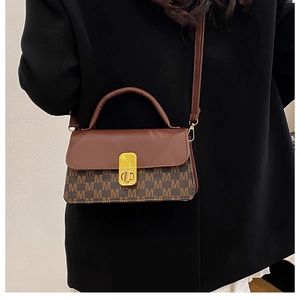 Detail of vintage brown M-pattern canvas bag with gold rotary lock on black blazer