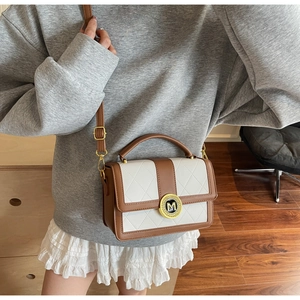 Detail of quilted white and brown crossbody bag with gold M-logo buckle and leather strap
