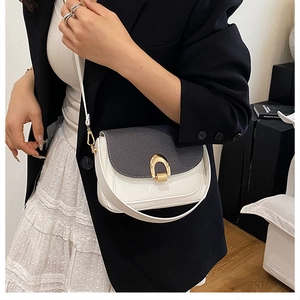 Gros plan du sac selle blanc avec rabat texturé gris et boucle dorée porté par un mannequin