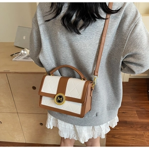 Detail of elegant two-tone leather handbag with rhombus stitching and golden M buckle