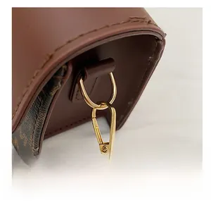 Macro shot of gold D-ring and lobster clasp on a dark brown luxury leather crossbody bag