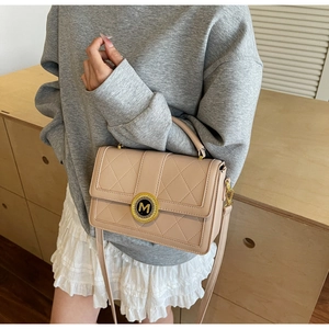 Close-up of beige quilted crossbody bag featuring a golden circular M-logo clasp