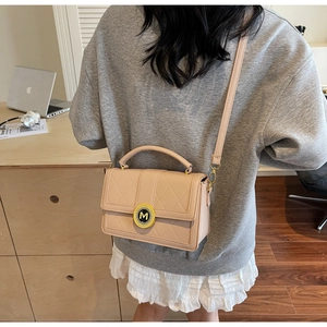 Detail of light beige quilted crossbody bag with golden M buckle worn by a woman