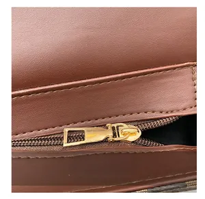 Detailed macro view of the smooth gold metal zipper and dark brown lychee leather texture