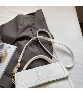 Detail of white quilted handbag featuring a golden letter M clasp and adjustable strap
