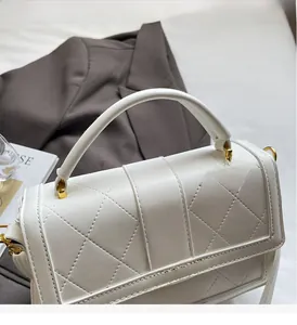 Close-up of white quilted leather handbag with gold M logo buckle and sturdy handle