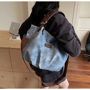 Detail of grey-blue canvas bucket bag showing leather strap and metal hardware details