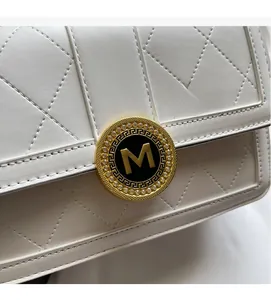 Detail showing the white quilted pattern and gold M logo buckle on the handbag
