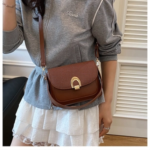 Détail d'un sac besace en cuir marron avec une boucle fer à cheval dorée en bandoulière
