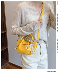 Détail d'un sac seau jaune à texture litchi avec nœud en dentelle et chaîne perle
