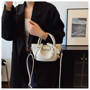 Détail du sac seau crème texturé litchi avec nœud en dentelle et chaîne perle