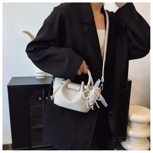 Détail du sac seau en cuir grainé avec nœud en dentelle et breloques en perles