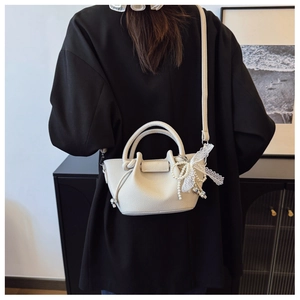 Sac seau chic en cuir crème avec nœud en dentelle porté par un mannequin élégant