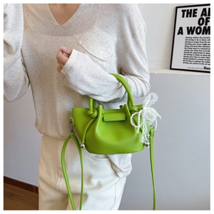 Détail du sac seau vert en cuir grainé avec perles décoratives et dentelle sur l'anse