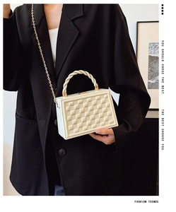 Detail of white geometric textured box bag with rope handle and gold chain strap