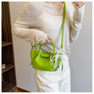 Détail du sac seau en cuir vert citron avec nœud en dentelle et breloque en perles