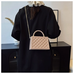 Quilted beige top-handle bag with gold chain strap on model in black blazer