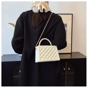 Detail of white quilted crossbody bag with golden chain and woven handle on a black blazer