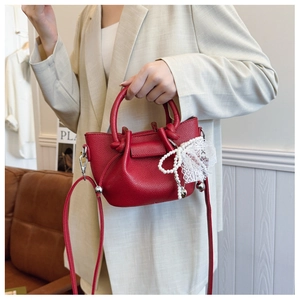 Détail du sac seau rouge à motif litchi avec breloque en perles et nœud en dentelle