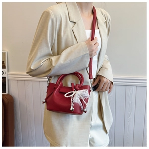 Détail du sac seau en cuir rouge avec dentelle et décoration de nœud en perles