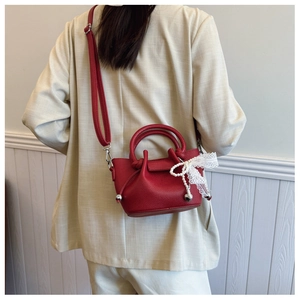 Gros plan du sac en cuir grainé rouge avec nœud en dentelle et pendentif cœur perlé