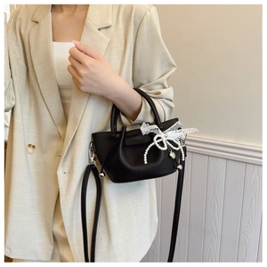 Détail du sac seau noir grainé avec nœud en dentelle et breloque perle en cœur