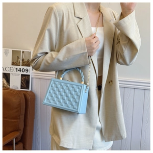 Close-up of light blue box bag with geometric texture and woven handle on model