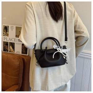 Détail du sac seau noir texture litchi avec pendentif perle et nœud en dentelle
