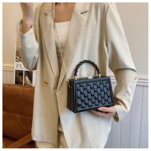 Detail of black box bag with relief pattern and woven handle worn on beige blazer