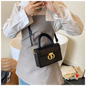 Dettaglio di una borsa box in pelle nera con chiusura a monogramma dorato e manico a mano