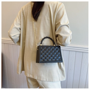 Detail of black quilted hard shell crossbody bag with woven handle and gold chain