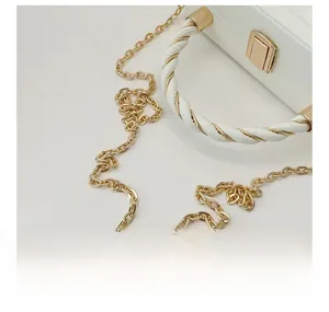 Close-up of golden metal chain and elegant leather handle on white crossbody bag