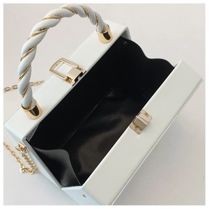 Macro view of white box bag featuring a metallic push-lock and elegant golden chain strap